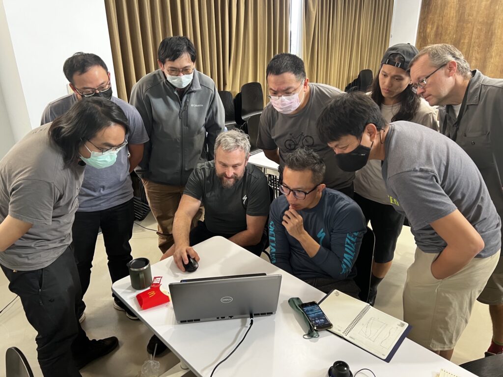An image of a man teaching a group of people gathered around a computer.