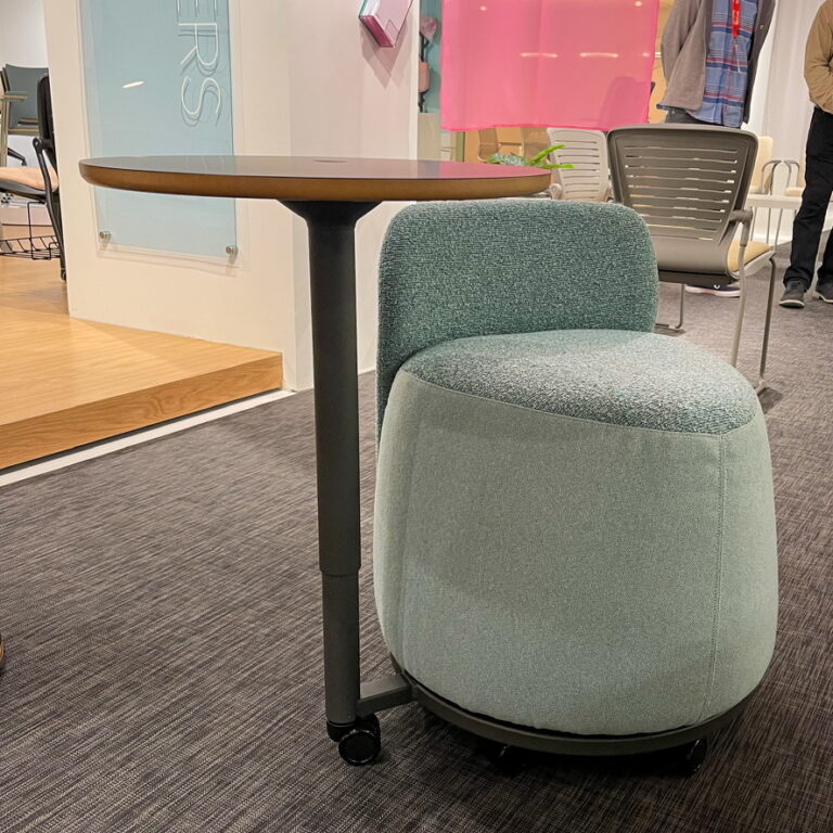 A teal designer chair with a desk attached from the Om Seating display at NeoCon 2023