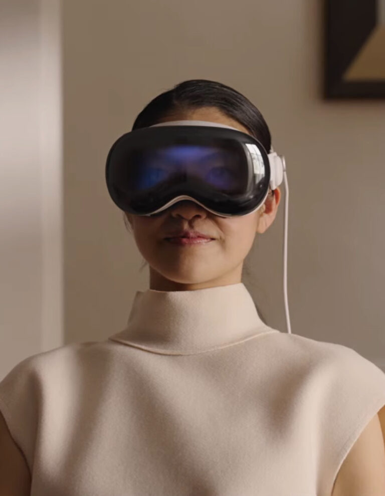 An image of a woman with dark hair and a cream blouse using the Apple Vision Pro VR headset.